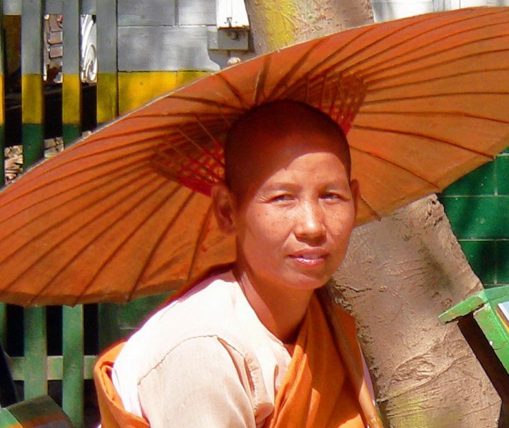 Novizin mit Sonnenschirm auf einer Parkbank in Mandalay Myanmar sitzend